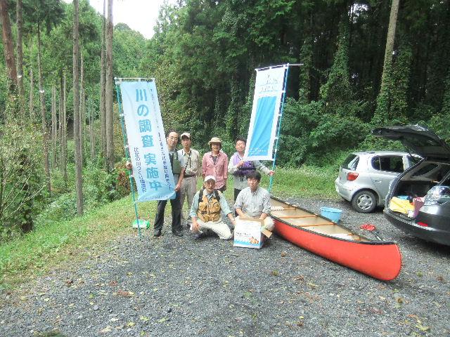 陸にあげたカヌーの横で、のぼり旗「川の調査実施中」を持って集合写真。６名。